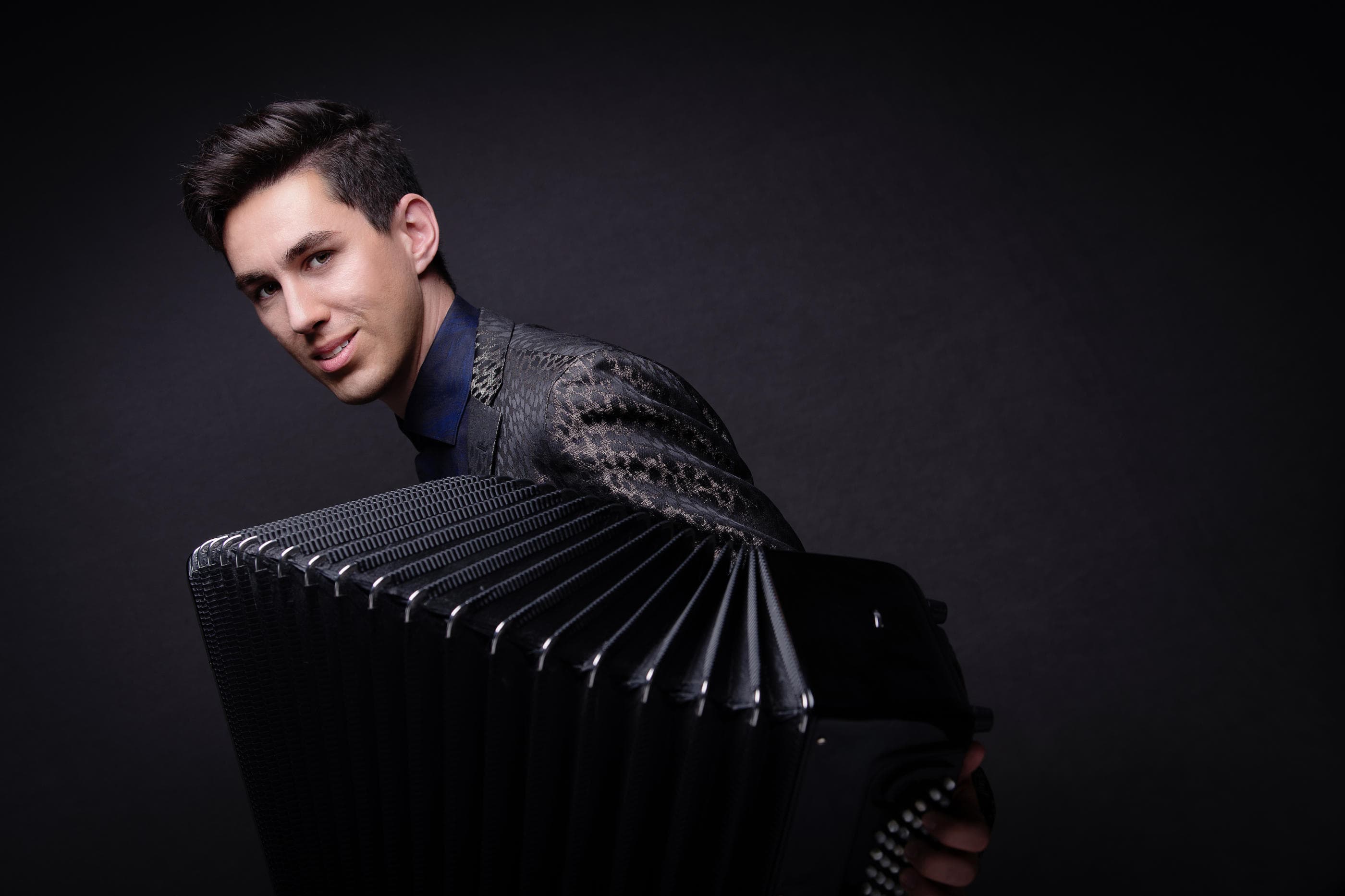 A photo of one of the members of Bridge and Wolak Duo, smiling while holding an accordion.