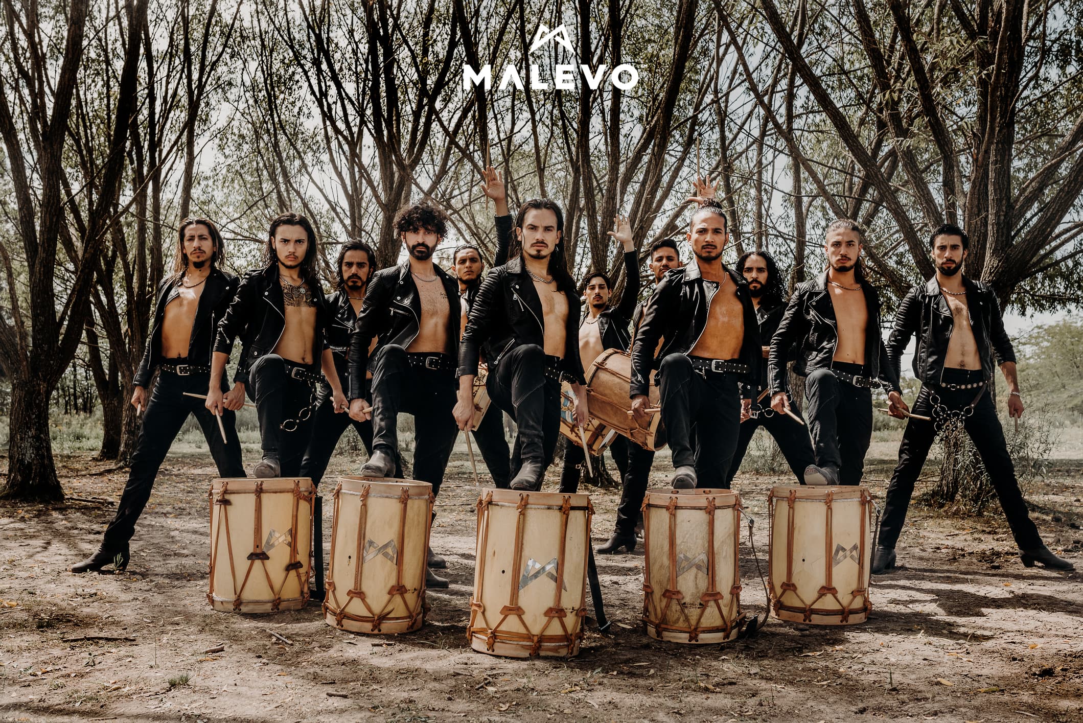 A photo of the twelve members of Malevo all dressed in black standing with their drums