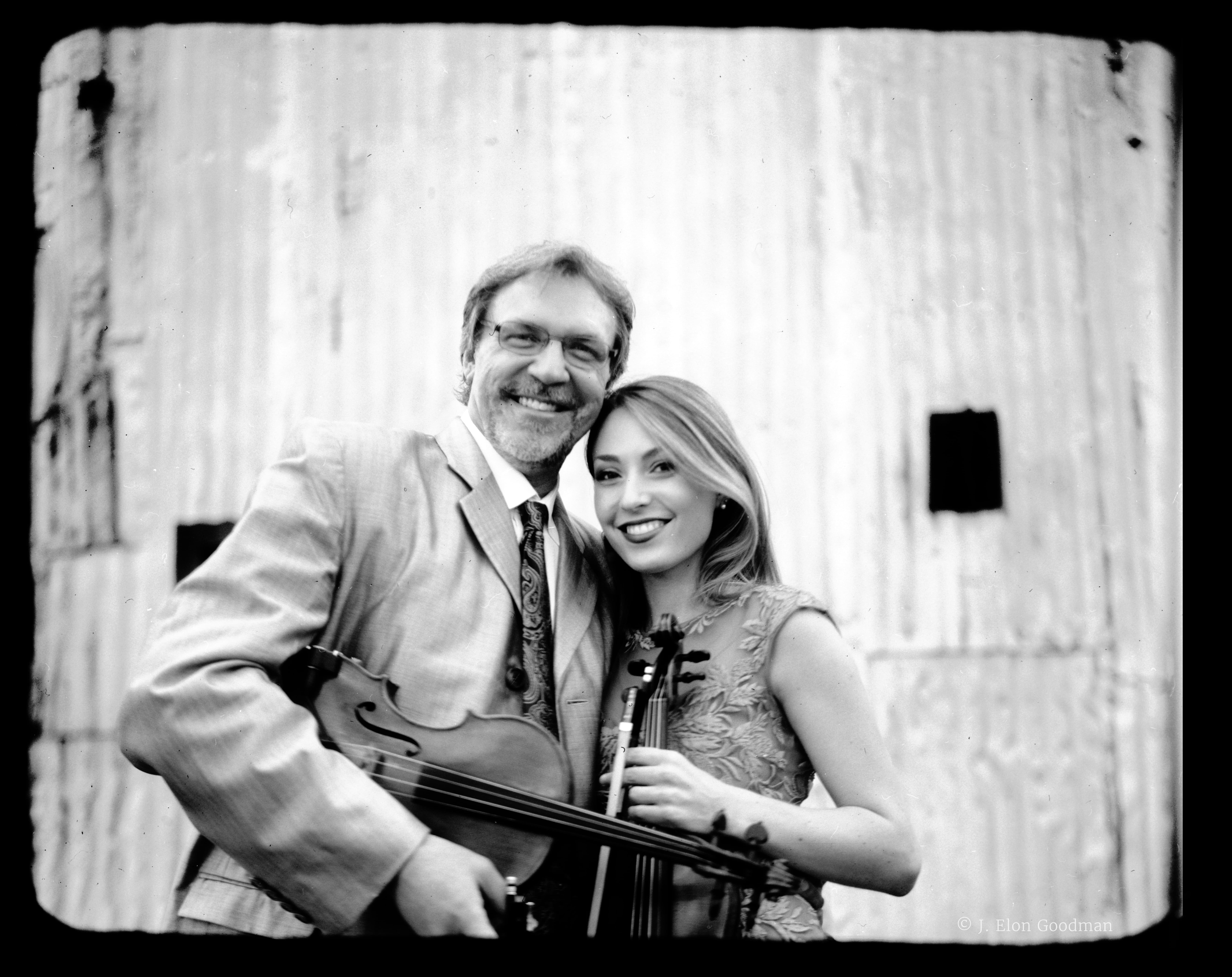 A black and white pictyure of Mark and Maggie standing together, holding their violins.
