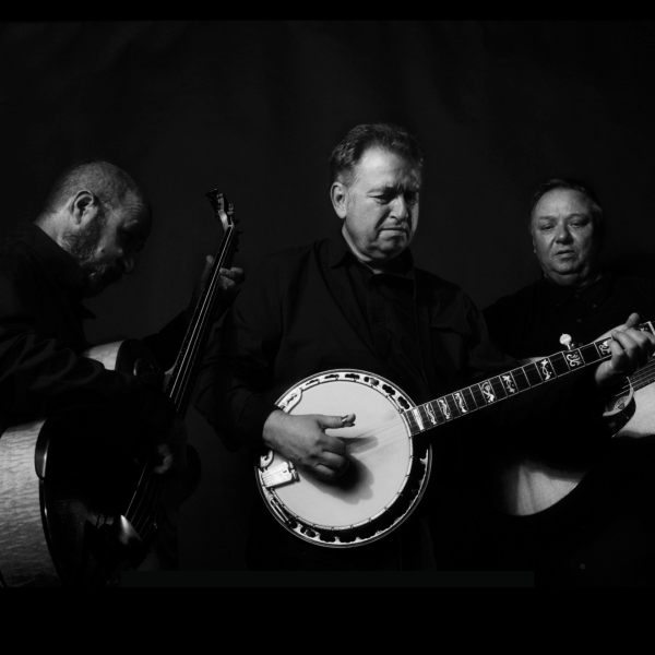 a black and white photo of three men dressed in black, a large accoustic bass is held by the man on the left, on the right is a man looking down at his accoustic guitar, and in the center a mn playing the banjo feels the emotions of the music